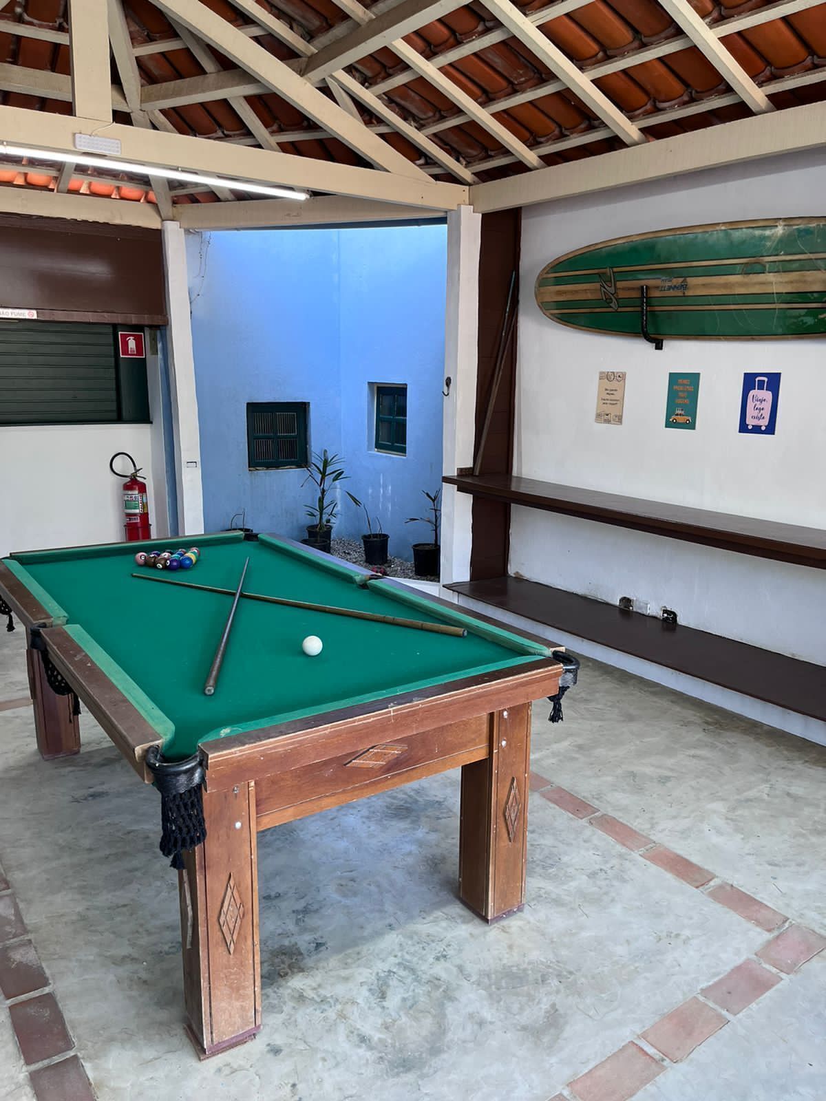 A pool table with balls, a fire extinguisher, and a surfboard on the wall.