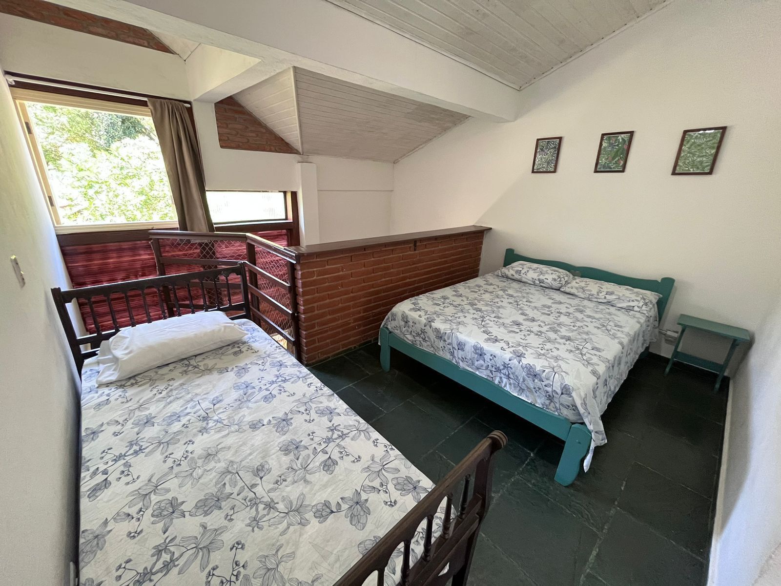 A dormitory room with two beds, a wooden headboard, a small table, and a window with curtains.