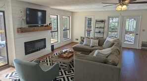 A spacious living room with a fireplace, a television mounted on the wall, a sofa, and a ceiling fan.