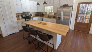 A modern kitchen with white cabinets, a wooden island with bar stools, stainless steel appliances, and pendant lighting. - Cedar Lake Retreat (Buckhead)