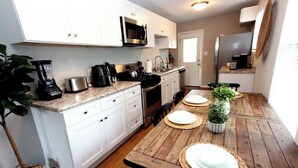Une cuisine compacte avec des meubles blancs, un four à micro-ondes, une cuisinière et une machine à café.