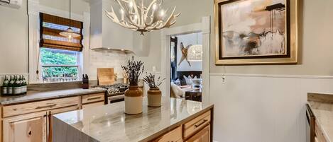 A kitchen with a marble island, wooden cabinets, a chandelier, and a framed abstract painting.