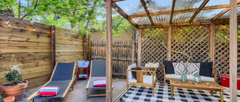A wooden pergola with a checkered floor, two lounge chairs, a small table, and a sofa with cushions.