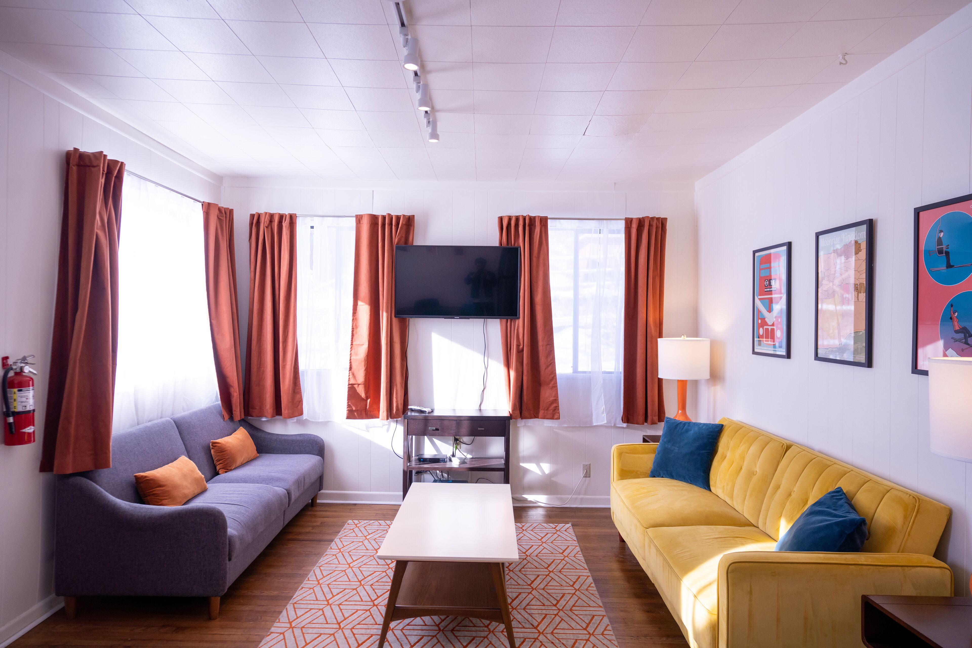 A modern living room with a sofa, a yellow couch, a flat-screen TV, and a coffee table.