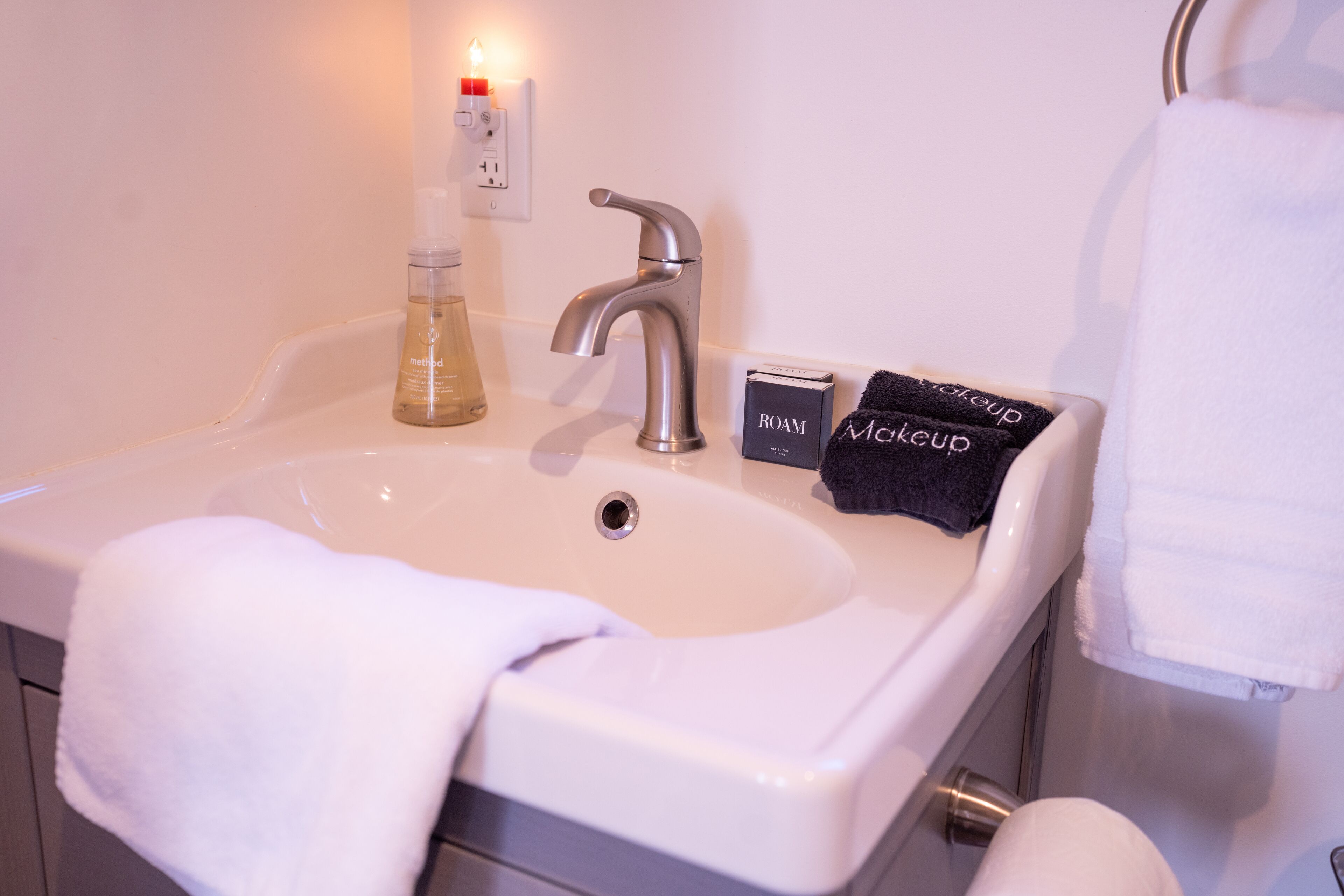 A bathroom sink with a mirror, a towel, a makeup box, and a bottle of liquid soap.