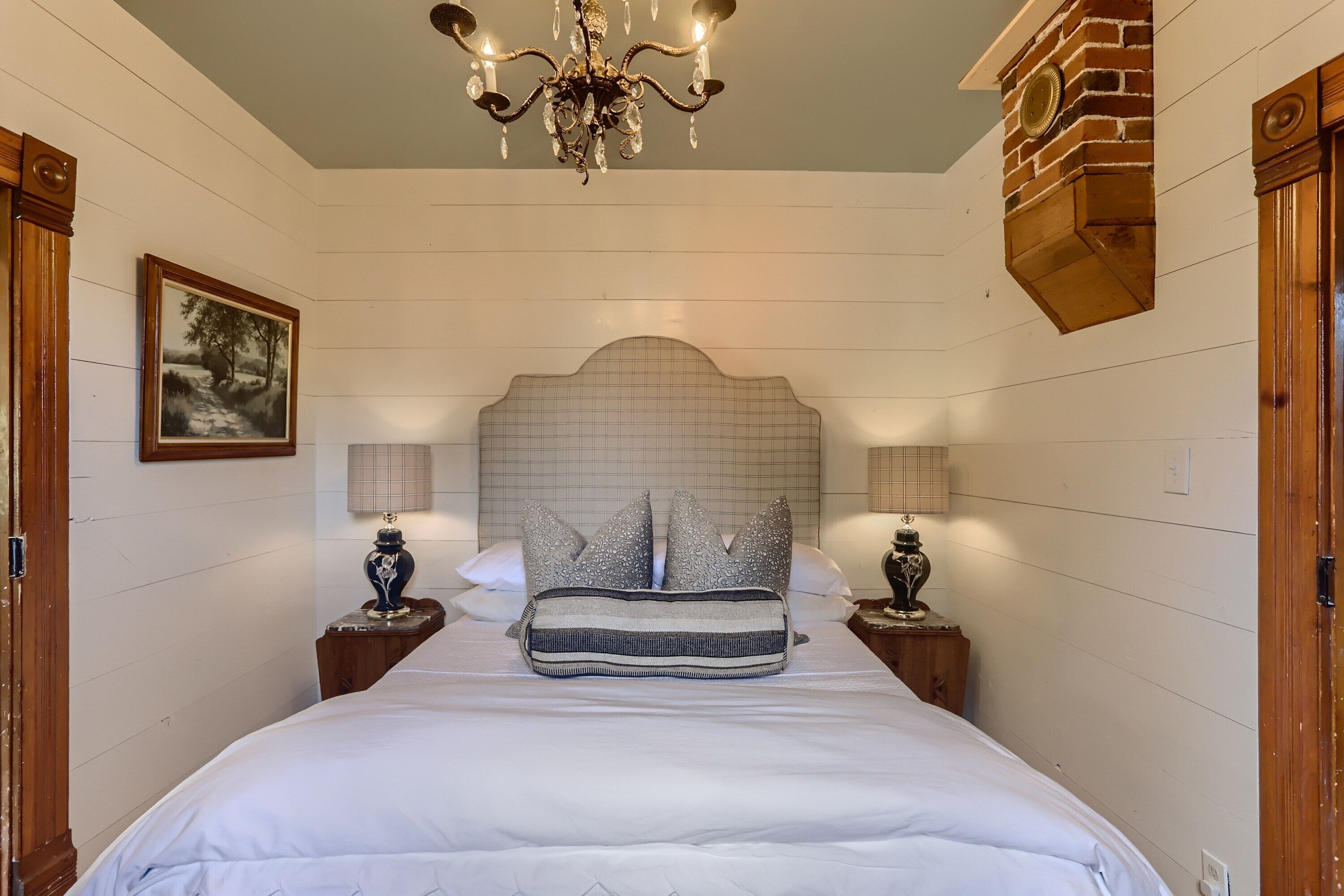 A bedroom with a large bed, a chandelier, a headboard with a grid pattern, and two bedside tables with lamps.