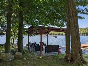 Un belvédère doté de sièges extérieurs, offrant une vue sur un lac où l’on aperçoit un bateau au loin.