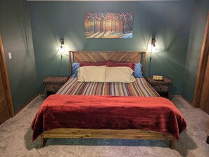A bedroom with a bed, two bedside tables, a nightstand, a painting on the wall, and a thermostat.