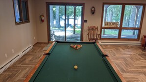 Een pooltafel met een witte biljartbal, een houten stoel en een bord met daarop een welkomstboodschap, nabij een groot raam.