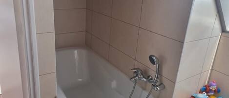 Ein Badezimmer mit einer Badewanne, einer Duschbrause und einem Regal mit Spielzeug.