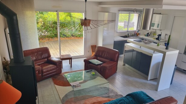 Ein modernes Wohnzimmer mit Kamin, Ledersofas, einem Glastisch und einer Küchenzeile mit Spüle und Schränken.