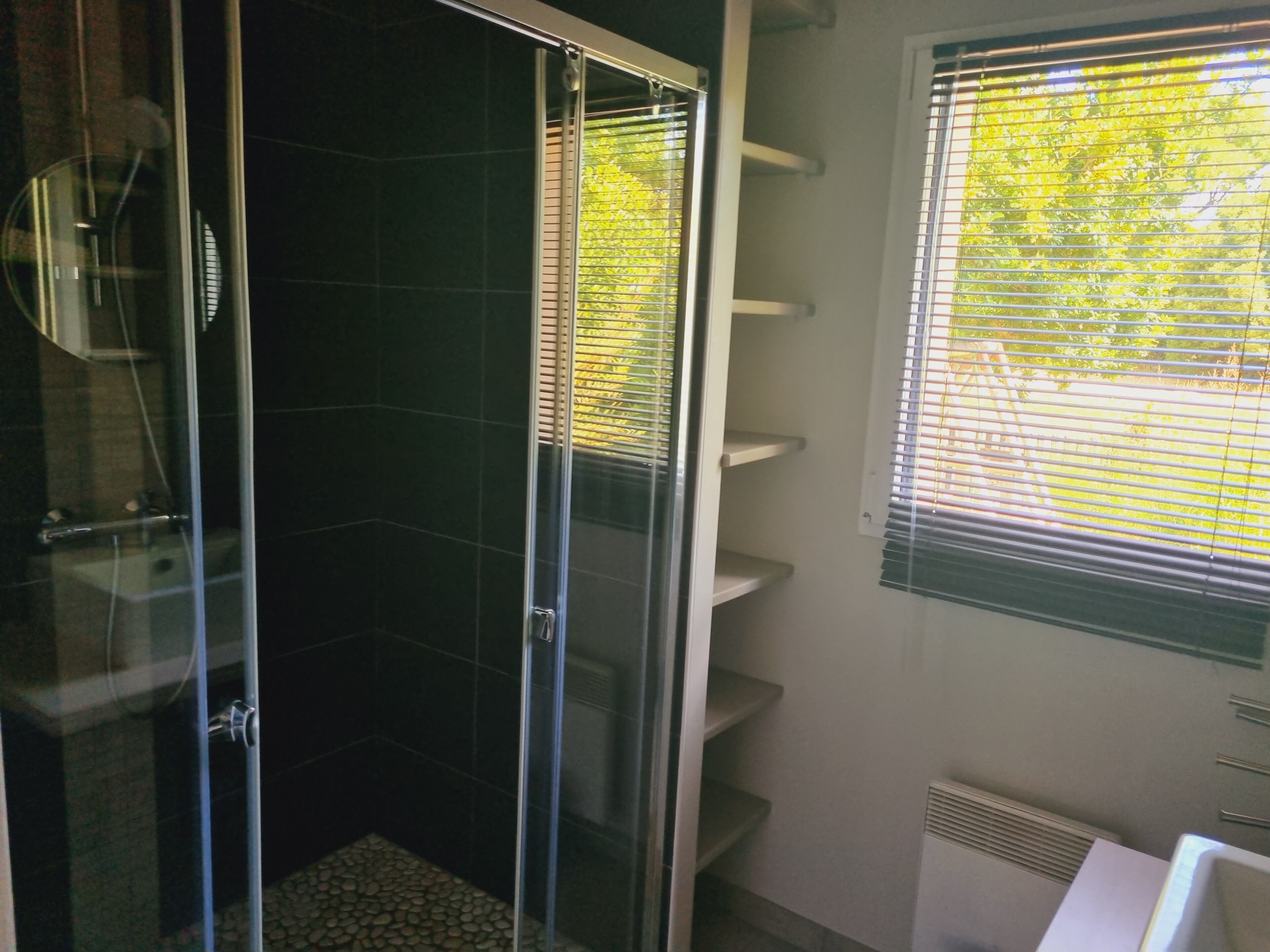 A bathroom with a glass-enclosed shower, a white sink, and a window with blinds.
