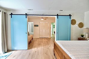 Une chambre à coucher comprenant un lit, une porte coulissante, un ventilateur de plafond et un couloir menant à une autre pièce.