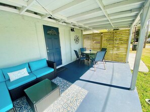 Un patio couvert comprenant un canapé bleu, une petite table et une table avec un plateau en verre, ainsi que des chaises.