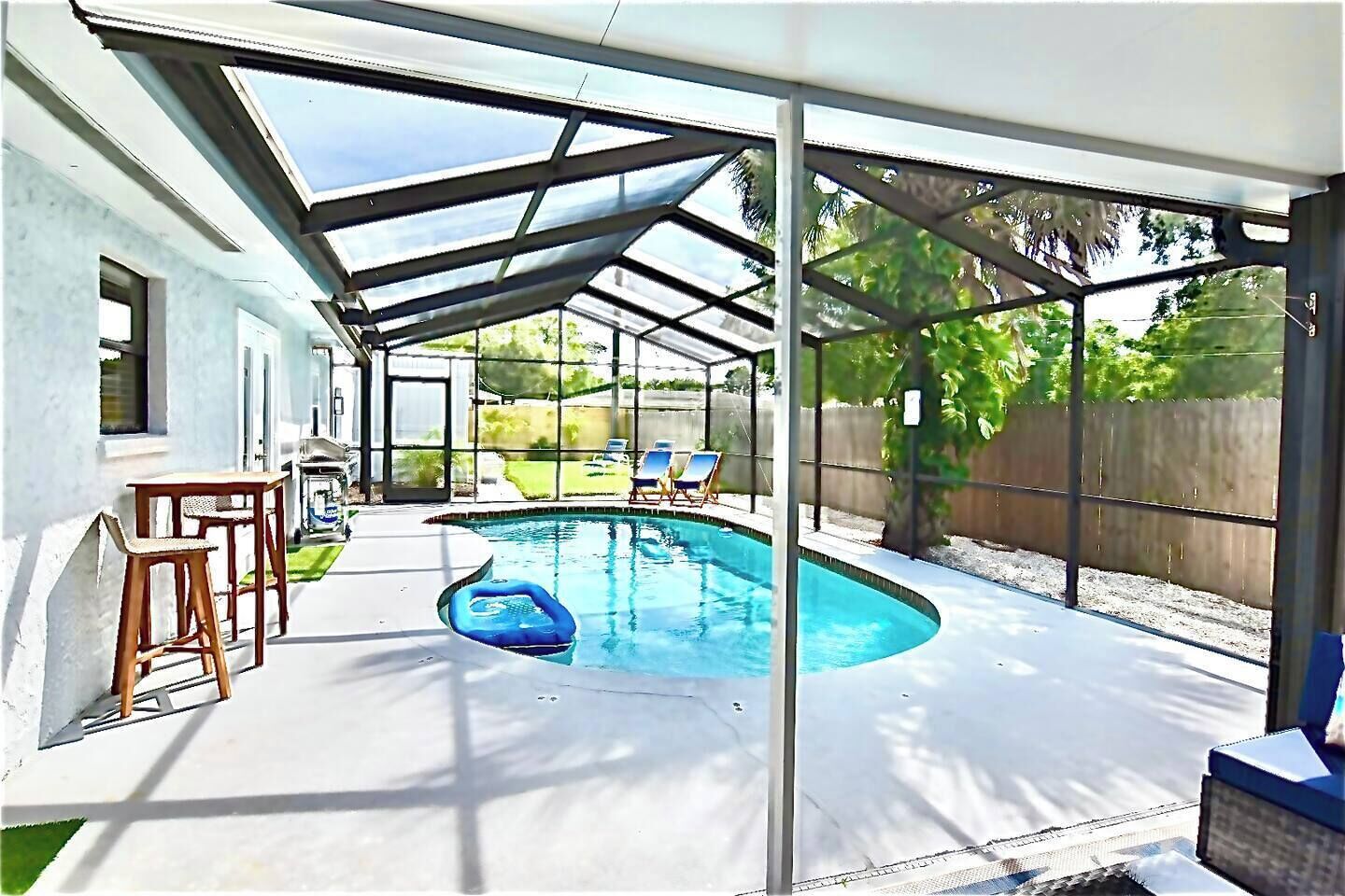 A covered outdoor swimming pool area with a patio, lounge chairs, and a small inflatable pool.