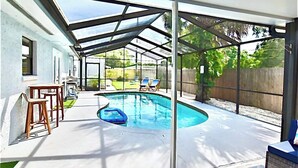 A covered outdoor swimming pool area with a patio, lounge chairs, and a small inflatable pool.