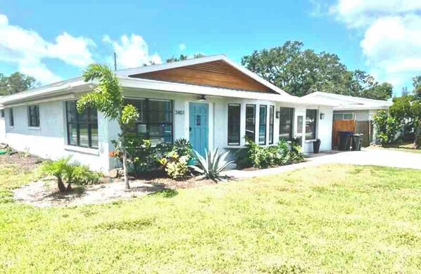 Une maison de plain-pied avec un porche à l’avant, un petit jardin et un ciel bleu dégagé.