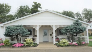 A white single-story building with a porch, two trees, and flower beds. - Country View Lodging In the heart of Amish Country (Baltic)