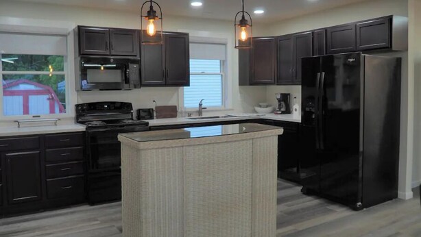 A modern kitchen with dark cabinets, a black refrigerator, a microwave, and a large island with a light-colored countertop. - Country View Lodging In the heart of Amish Country (Baltic)