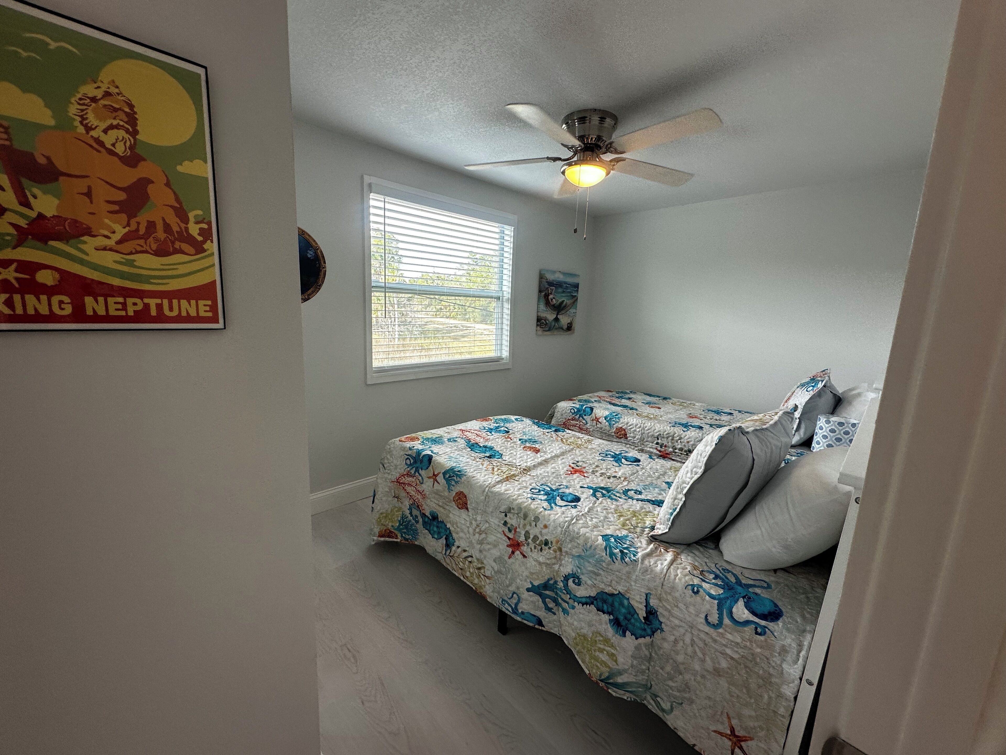 A bedroom with two beds, a ceiling fan, a window with blinds, and a poster on the wall.