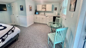 A compact room with a bed, kitchenette, and a small dining area with a glass table and chairs. - Neptune's Grotto Waterfront Retreat (Spring Hill)