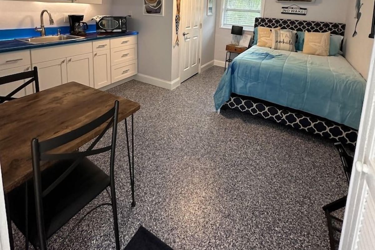 A compact room with a kitchenette, a bed with patterned bedding, and a dining area.