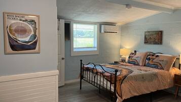 Une chambre à coucher avec un lit, une fenêtre, un climatiseur fixé au mur et un tableau encadré.