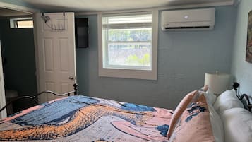 A bedroom with a bed, a window, an air conditioner, and a door.