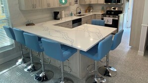 A modern kitchen with a marble island, blue bar stools, stainless steel appliances, and wooden cabinets. - Neptune's Grotto Waterfront Retreat (Spring Hill)
