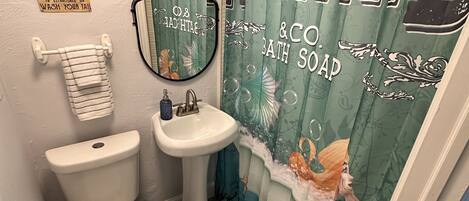 A bathroom with a toilet, sink, and shower curtain featuring a mermaid theme.