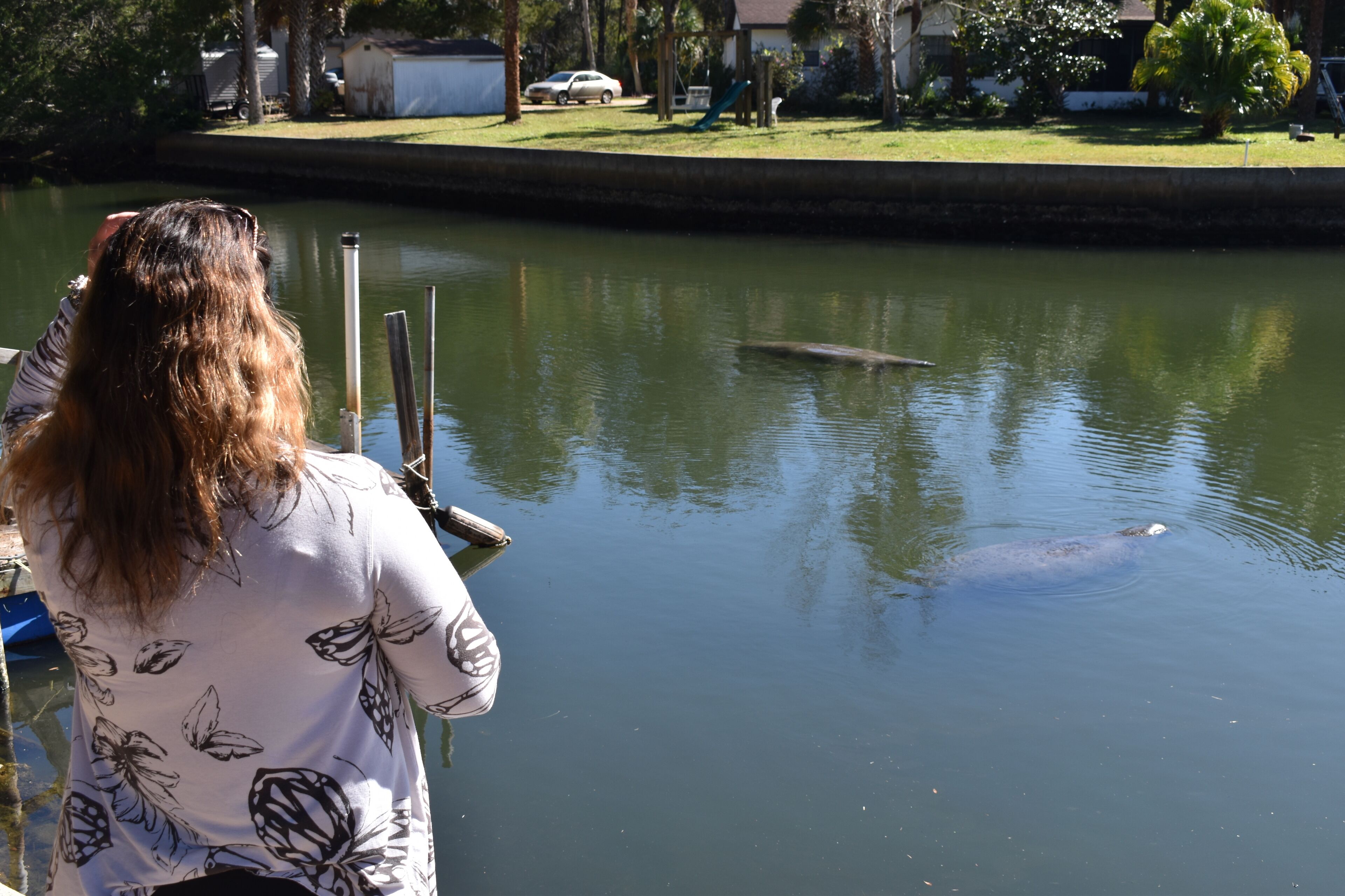 A person standing by a calm body of water with a boat docked nearby.