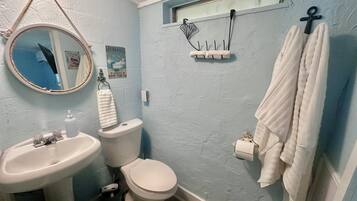 A bathroom with a sink, toilet, and a mirror. There is a towel rack with a towel hanging on it.