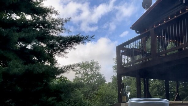 A person holding a glass of water in a hot tub with a wooden deck and trees in the background. - SkyBarn on Rocky Knob - Views, Relaxation, Adventure, Game Room & Hot Tub (Zionville)