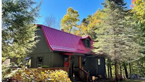 A cabin with a red roof, surrounded by trees and a grassy yard. - SkyBarn on Rocky Knob - Views, Relaxation, Adventure, Game Room & Hot Tub (Zionville)