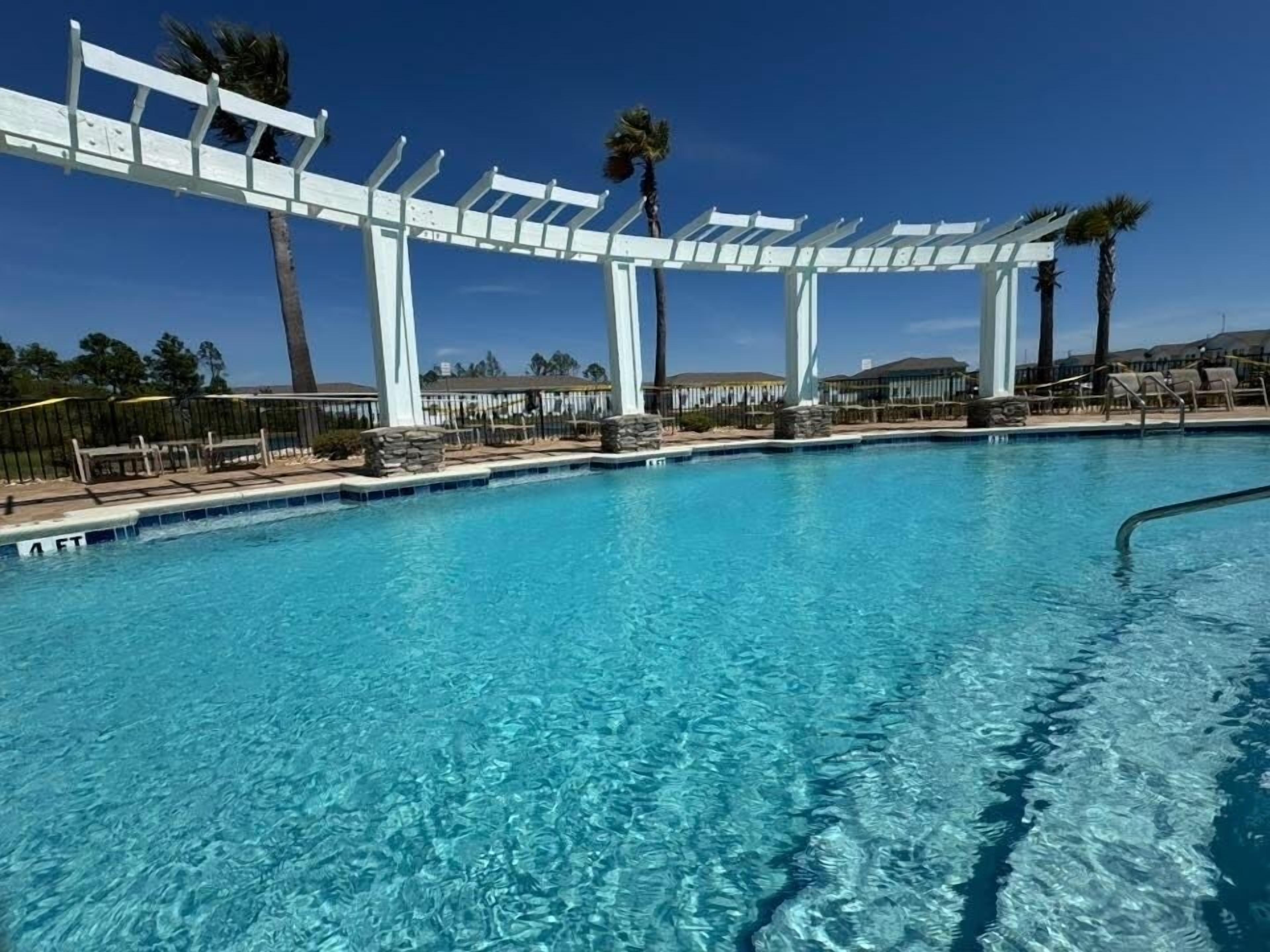 Ein klares, blaues Schwimmbecken mit weißen Pergolen und Palmen im Hintergrund.