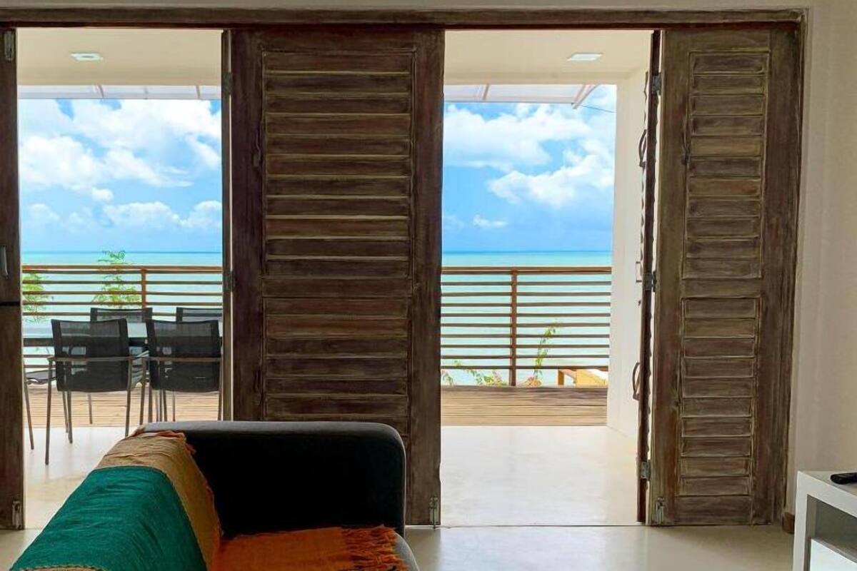 A room with a large sliding door leading to a balcony with a view of the sea.