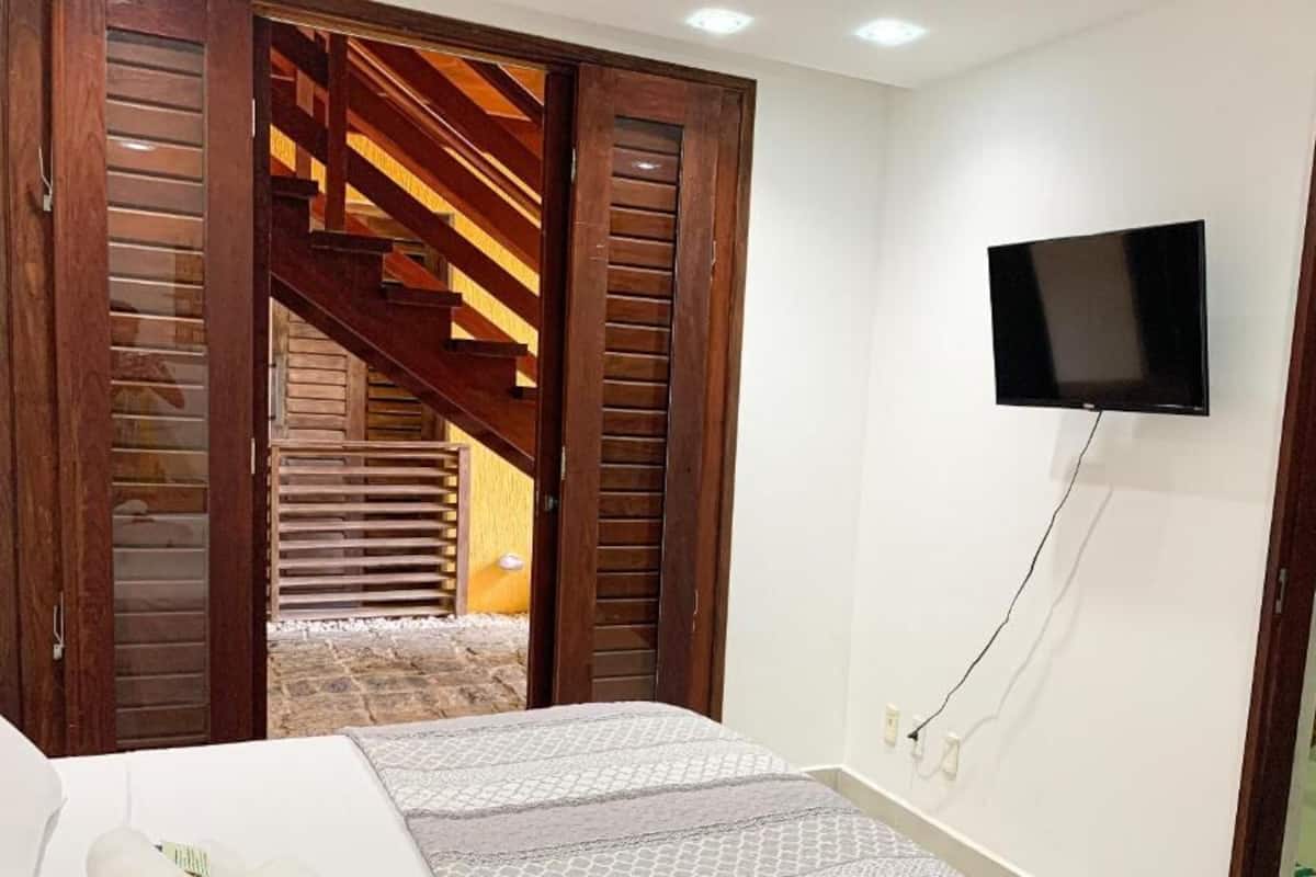 A bedroom with a bed, a TV mounted on the wall, and a wooden staircase leading to another room.