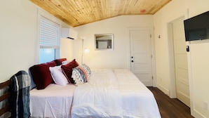 A bedroom with a wooden ceiling, a bed with white bedding, a red pillow, a bedside lamp, and a door with a mirror. - Breathtaking Views!  (Matlacha)