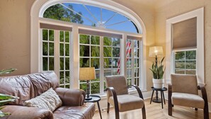 A room with a leather sofa, two armchairs, a small table with a lamp, and a large window with a view of greenery. - 2x Properties + Pool + Pet Friendly (Lakeland)