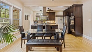 A spacious dining area with a glass table and dark chairs, a kitchen with dark cabinets and stainless steel appliances, and a ceiling fan. - 2x Properties + Pool + Pet Friendly (Lakeland)