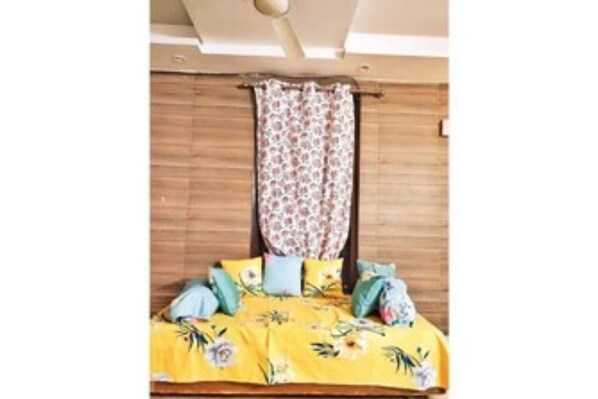 A room with a bed covered in yellow floral bedding, a wooden headboard, and a window with patterned curtains.