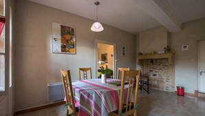 Un comedor con una mesa dispuesta para cuatro, sillas de madera, una lámpara colgante, una chimenea de piedra y un cartel en la pared.