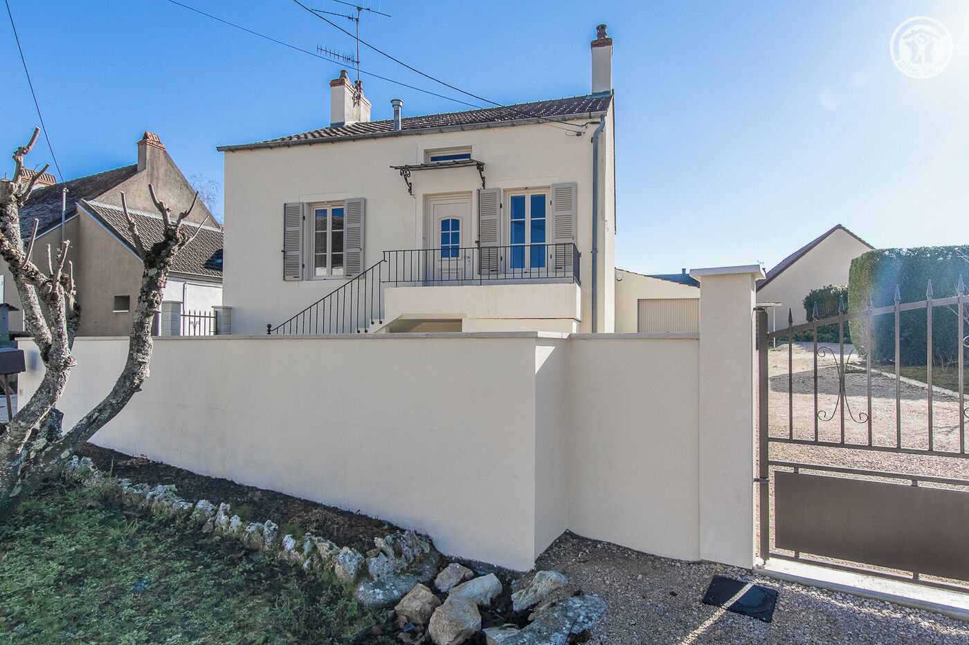 A two-story house with a balcony, a gated driveway, and a small garden area.