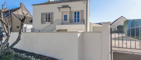A two-story house with a balcony, a gated driveway, and a small garden area.