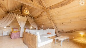 A cozy attic bedroom with a large wicker sofa, a small table, and a canopy bed. - Une Pause à Outry - Ozenay (OZENAY)
