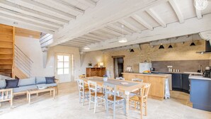 A spacious living area with a wooden staircase, a dining table with chairs, and a kitchen area with a sink and stove. - Une Pause à Outry - Ozenay (OZENAY)