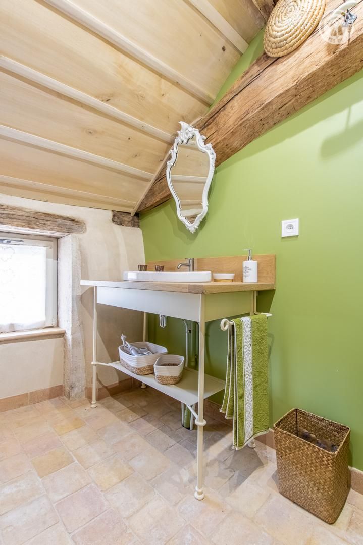 Une salle de bain avec un plafond en bois, un lavabo blanc, un miroir et un mur vert.
