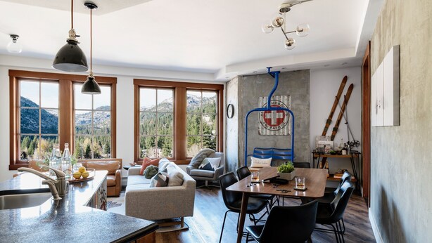 Eine moderne Küche mit einer großen Kochinsel, Essbereich mit schwarzen Stühlen und Blick auf Berge durch große Fenster.