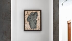 Eine hölzerne Bank mit einem geflochtenen Korb darunter, eine gerahmte Karte an der Wand und ein rotes Kissen.