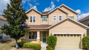 A two-story residential house with a beige exterior, a green front door, and a garage.